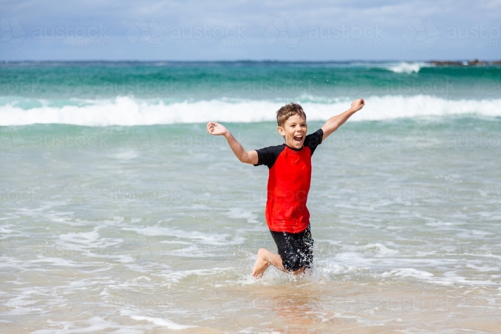 Happy kid running and splashing in seaside waves at the beach - Australian Stock Image