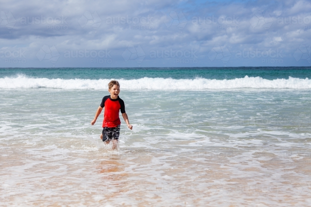 Happy kid running and splashing in seaside waves at the beach - Australian Stock Image