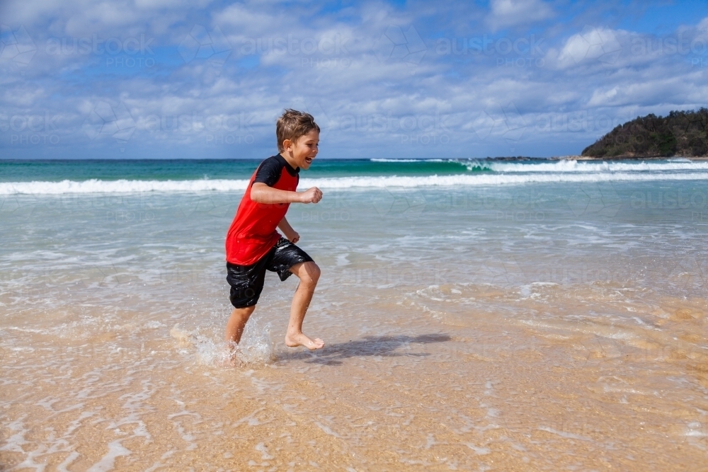 Happy kid running and splashing in seaside waves at the beach - Australian Stock Image