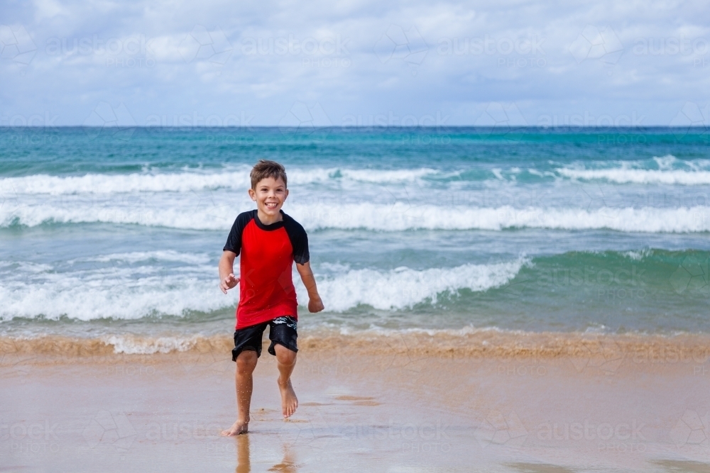 Happy kid running and splashing in seaside waves at the beach - Australian Stock Image