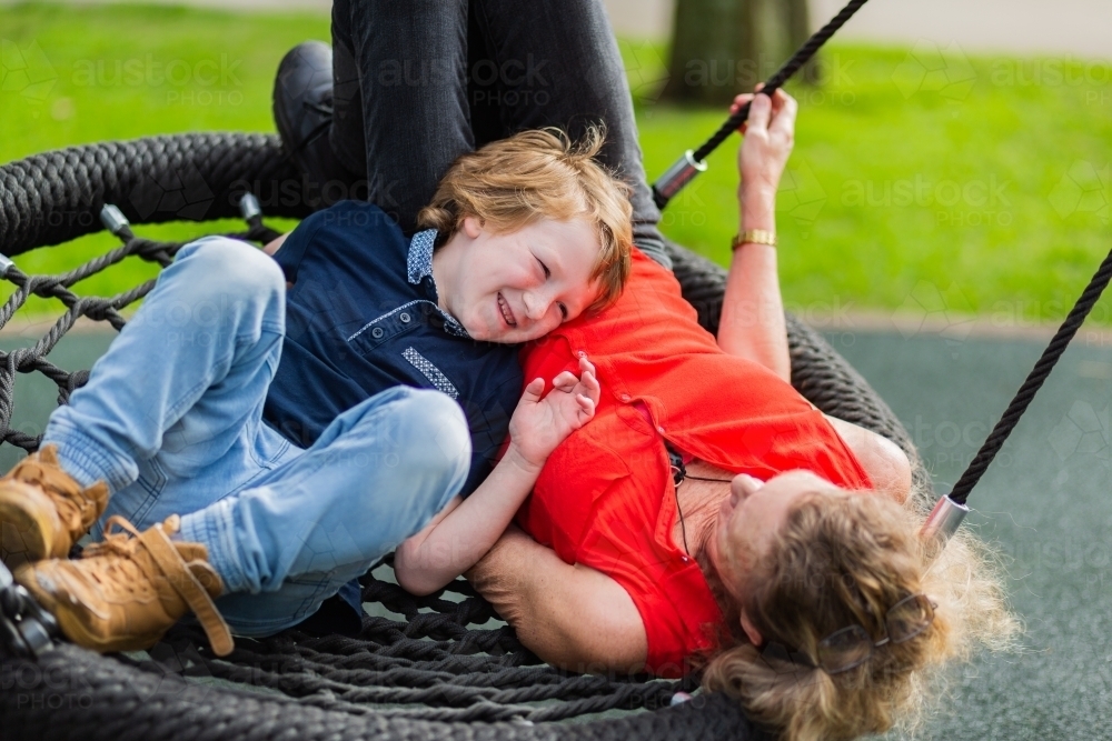 happy kid with grandmother lying on a swing at the park - Australian Stock Image