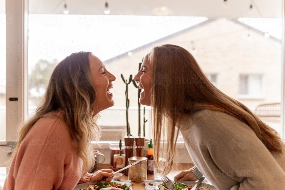 Happy, laughing female same sex couple at the dining table with their faces close to one other - Australian Stock Image