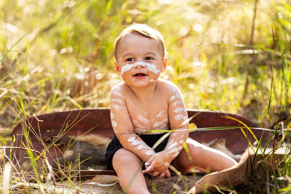 Happy little Aboriginal toddler boy sitting in coolamon in Australian bushland - Australian Stock Image