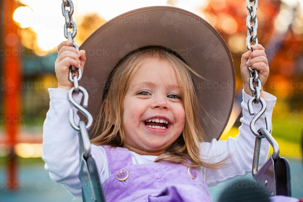 Happy little Australian girl laughing as she swings on swing at park playground - Australian Stock Image