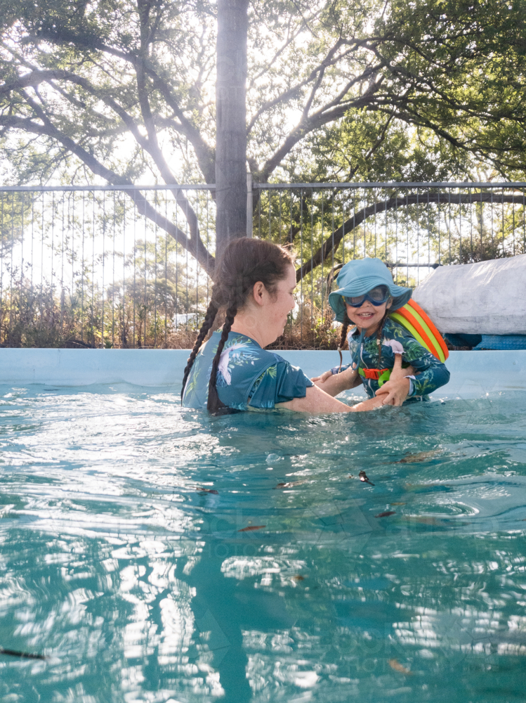Happy little Australian girl swimming in family backyard pool with mother enjoying summer - Australian Stock Image