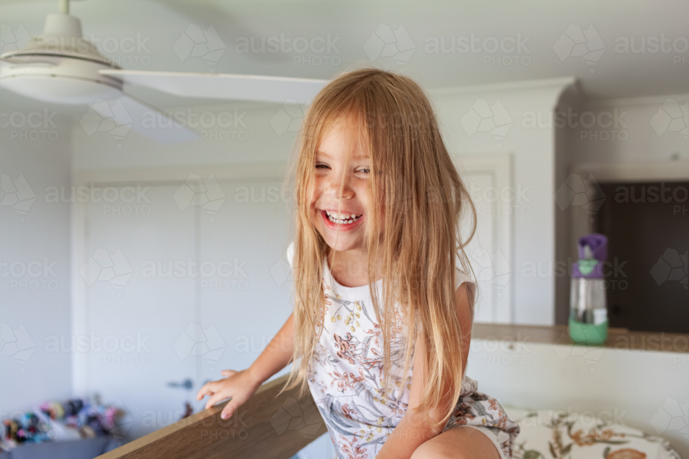 Happy little Australian girl with messy hair in her bedroom sitting on bunk bed in the morning - Australian Stock Image