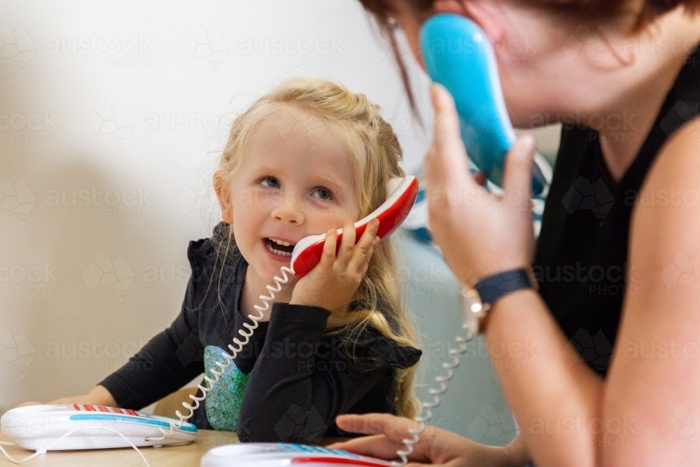 Happy little girl and mother speaking on toy phone - Australian Stock Image