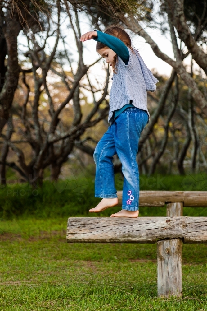 Happy little girl balancing on a pole outside near forest - Australian Stock Image