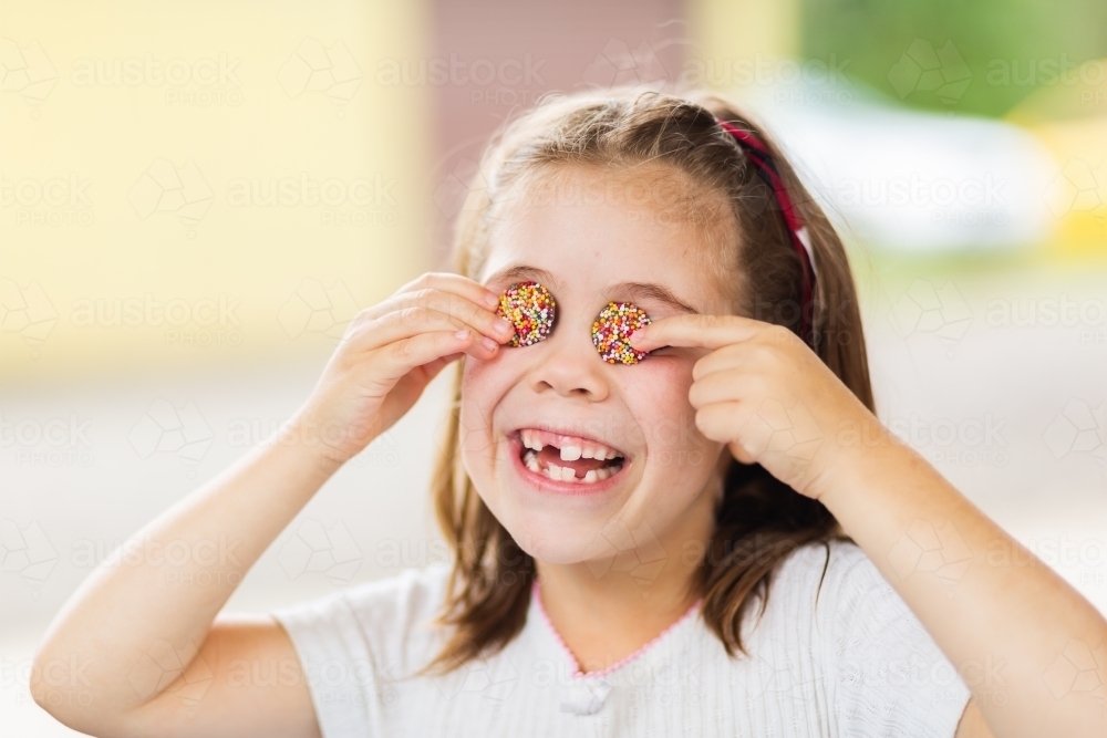 Happy little girl being silly with chocolate freckles on her face - Australian Stock Image