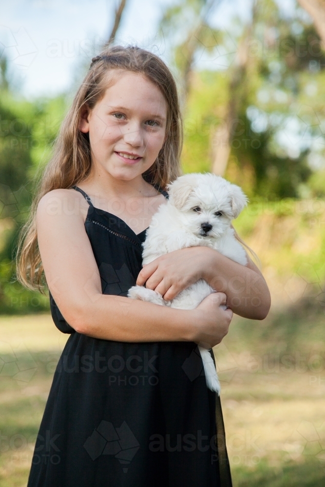 Happy little girl cuddling fluffy puppy - Australian Stock Image
