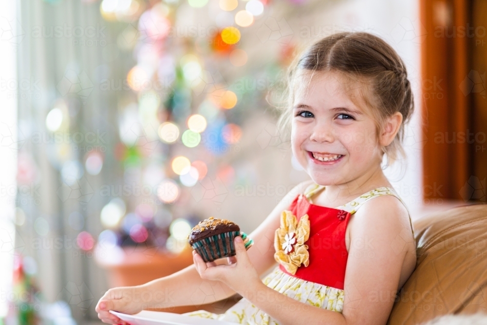 Happy little girl eating Christmas cupcake and smiling - Australian Stock Image
