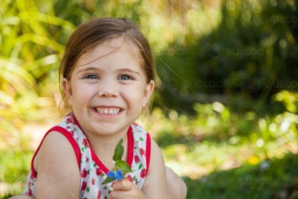 Happy little girl holding flower of wandering jew plant - Australian Stock Image