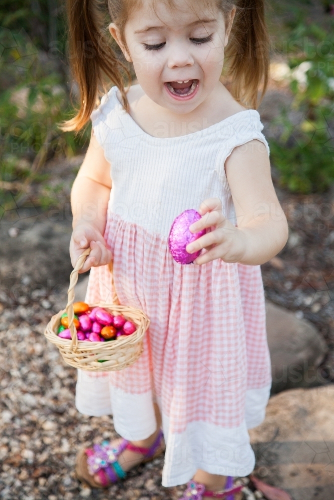 Happy little girl holding out pink Easter eggs - Australian Stock Image