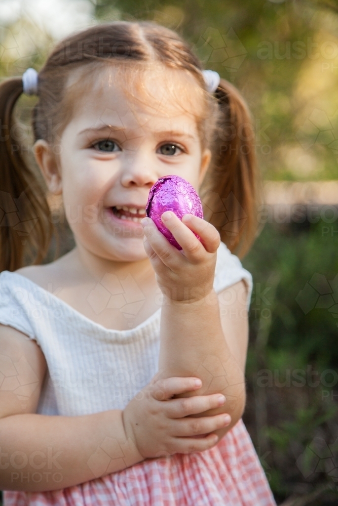 Happy little girl holding out pink Easter eggs - Australian Stock Image