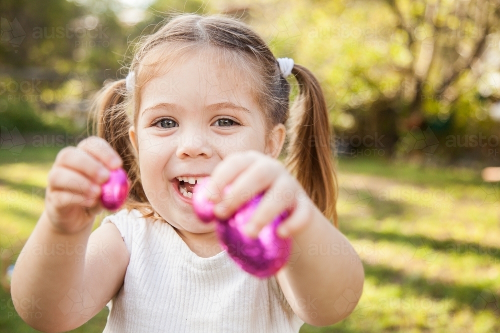 Happy little girl holding out pink Easter eggs - Australian Stock Image