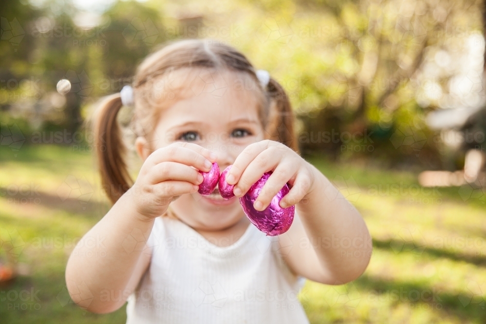 Happy little girl holding out pink Easter eggs - Australian Stock Image