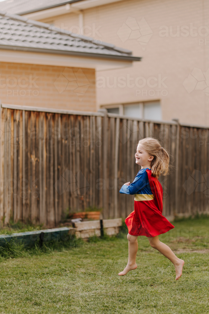 Happy little girl in a superhero costume running around backyard - Australian Stock Image