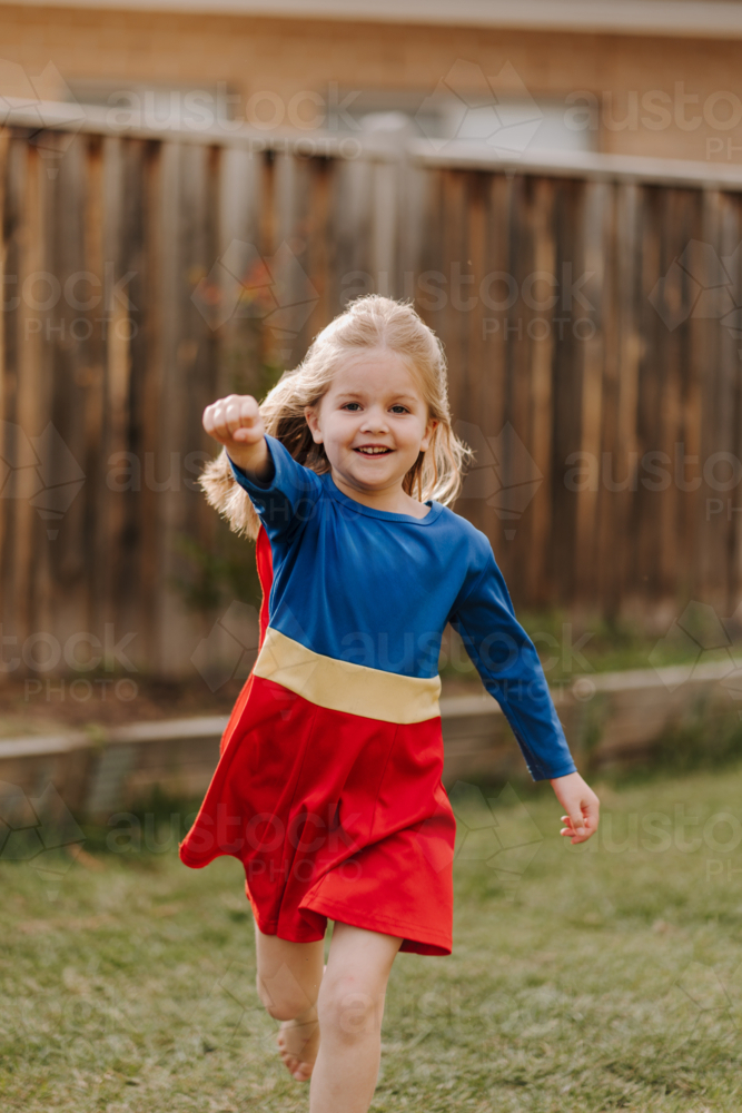 Happy little girl in a superhero costume running around backyard - Australian Stock Image