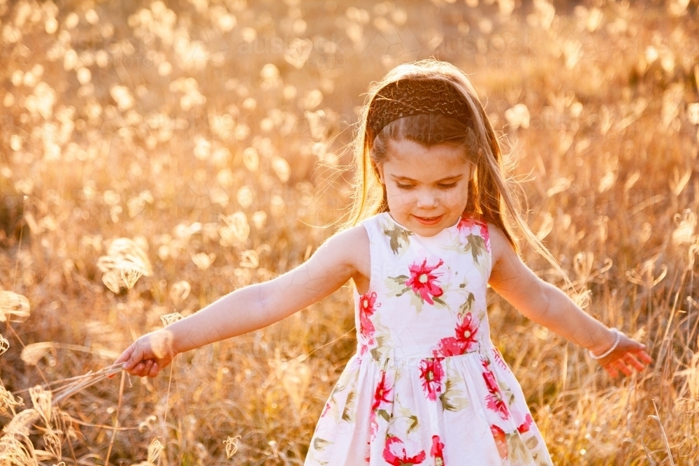 Happy little girl laughing and spinning in sunlit grass - Australian Stock Image