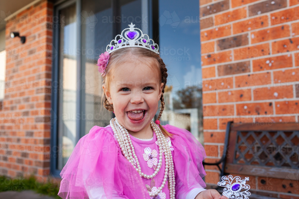 Happy little girl playing dressup with pink princess dress and crown in backyard - Australian Stock Image