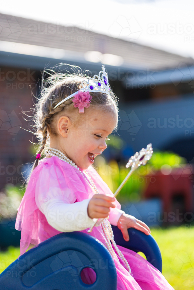 Happy little girl playing Dressup with pink princess dress and crown in backyard - Australian Stock Image