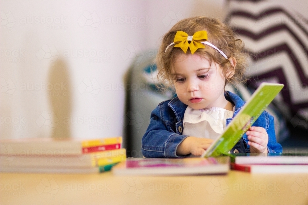 Happy little girl reading board books at table - Australian Stock Image