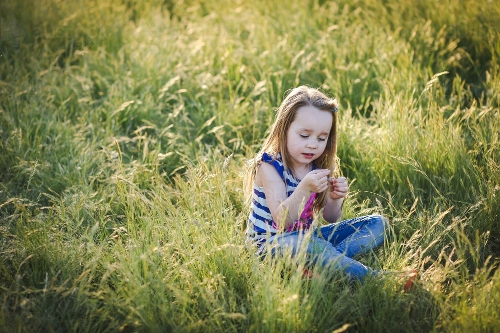 Image of Happy little girl sitting in long grass at the park. Outdoor ...