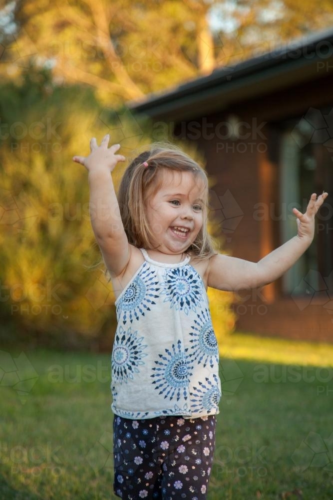 Happy little girl throwing grass into the air - Australian Stock Image