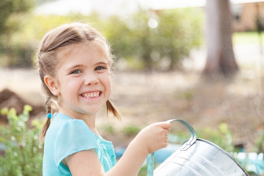 Happy little girl watering garden outside with watering can - Australian Stock Image
