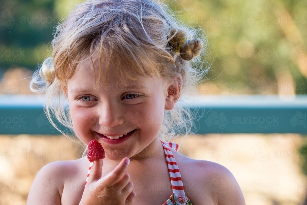 Happy little girl with a fresh red raspberry - Australian Stock Image