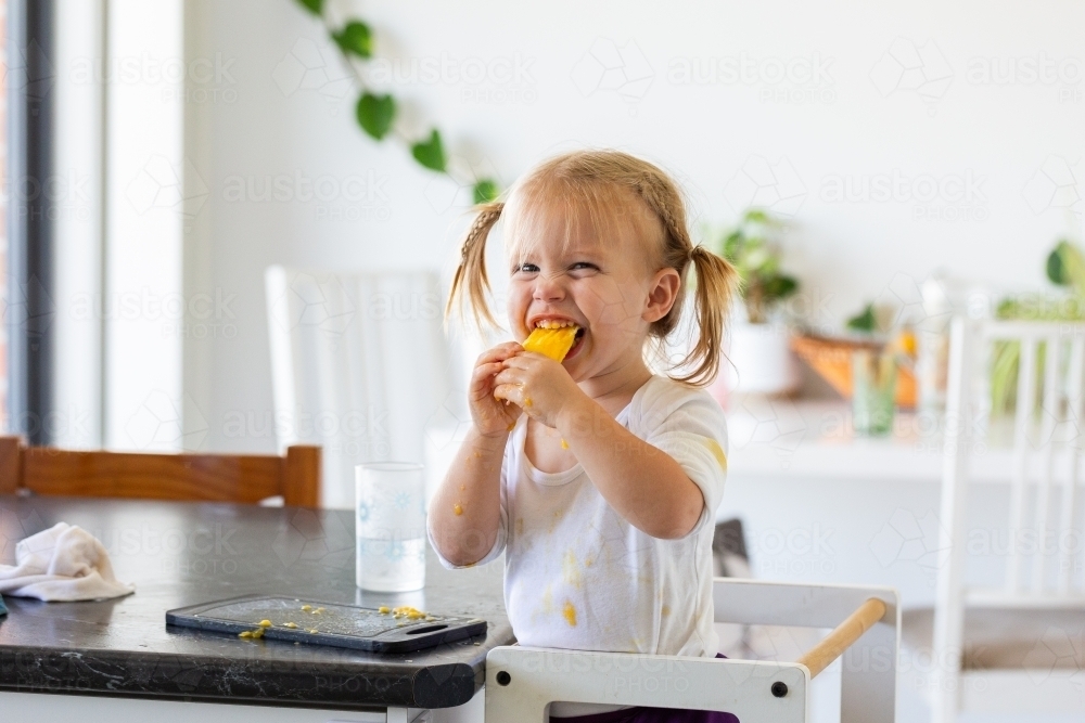 Happy little kid eating mango seed and getting sticky - Australian Stock Image