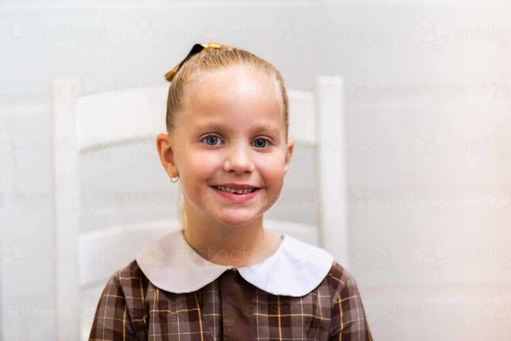 Happy little school kid smiling indoors on white chair - Australian Stock Image