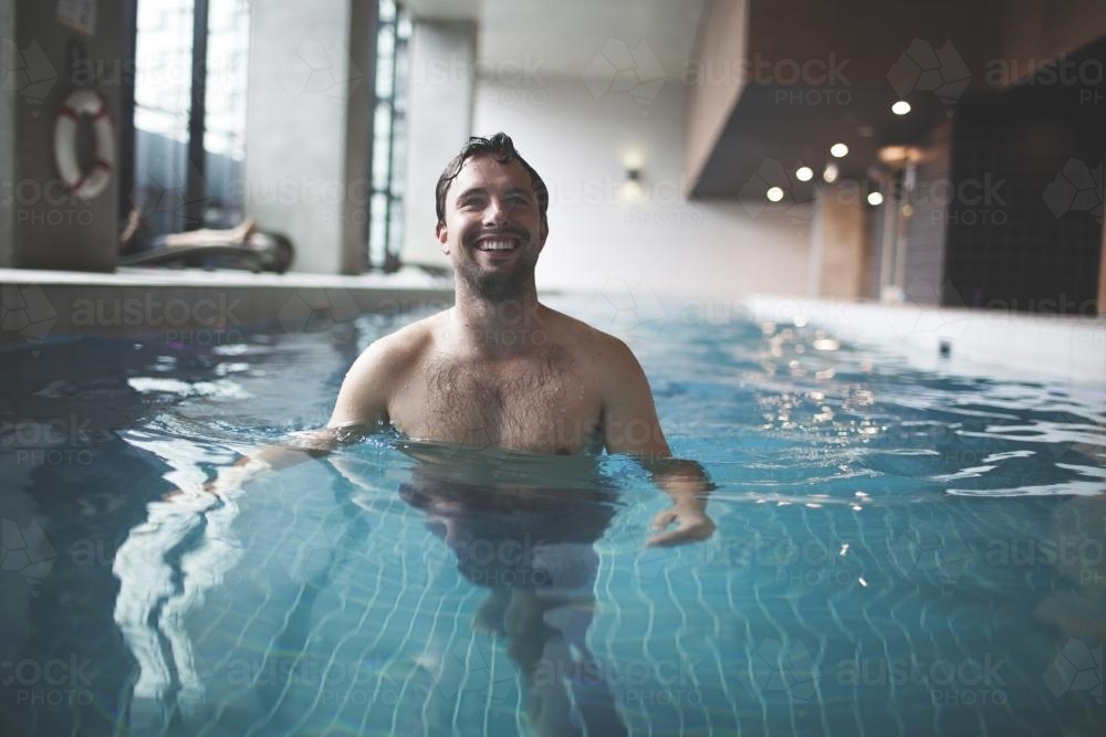 Happy male swimmer enjoying contemporary indoor lap pool - Australian Stock Image