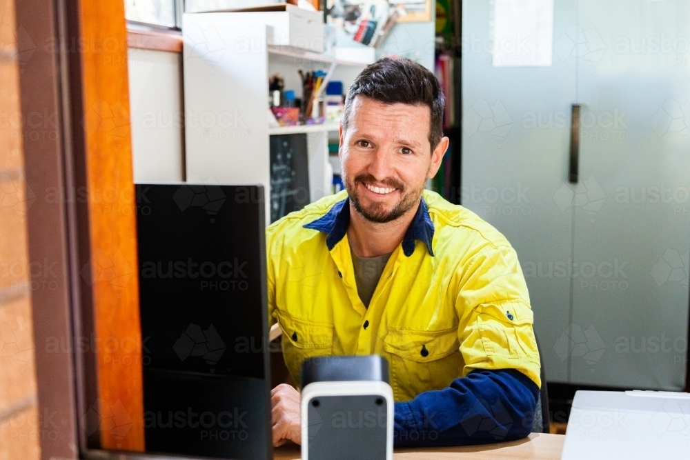 Happy male tradie at computer in home office - Australian Stock Image