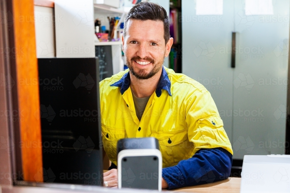 Happy male tradie at computer in home office - Australian Stock Image