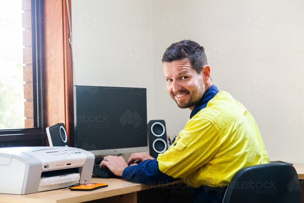 Happy male tradie at computer in home office - Australian Stock Image