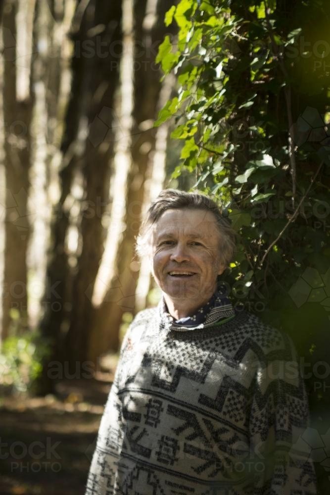 Happy man leaning against a vine covered tree in the park - Australian Stock Image