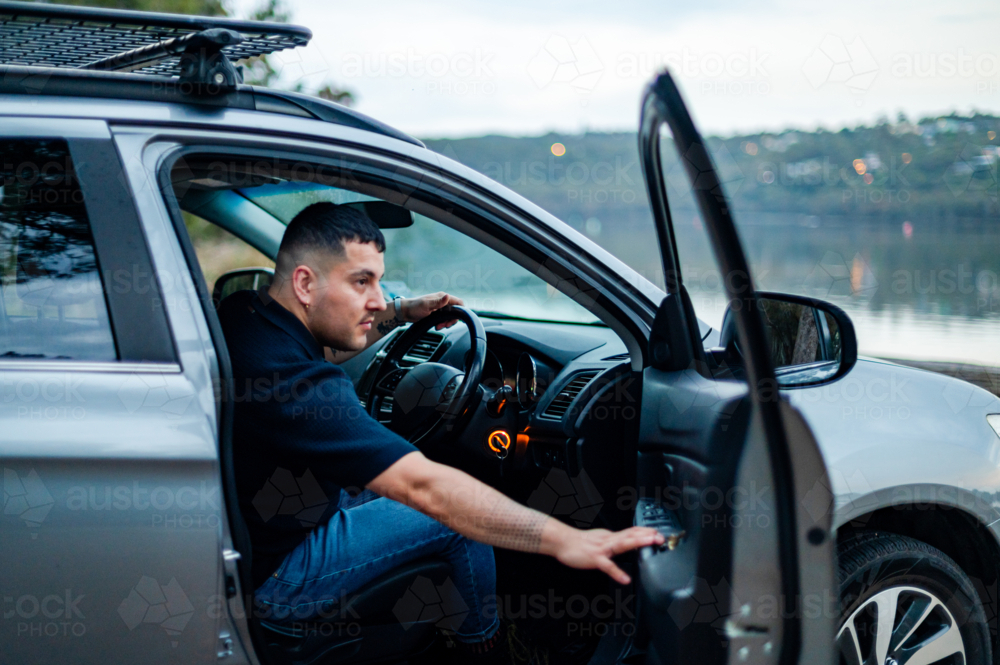 Happy man steps out of his car to enjoy a serene view by the water in a park setting. - Australian Stock Image