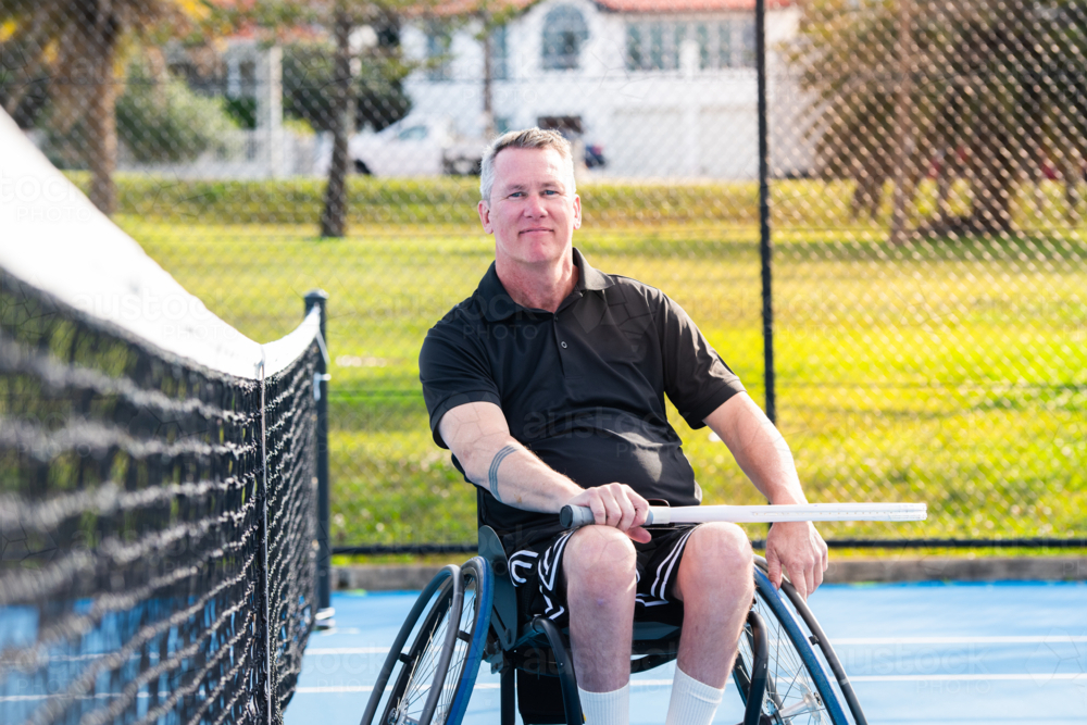 happy man with a disability is on tennis court in a wheelchair - Australian Stock Image