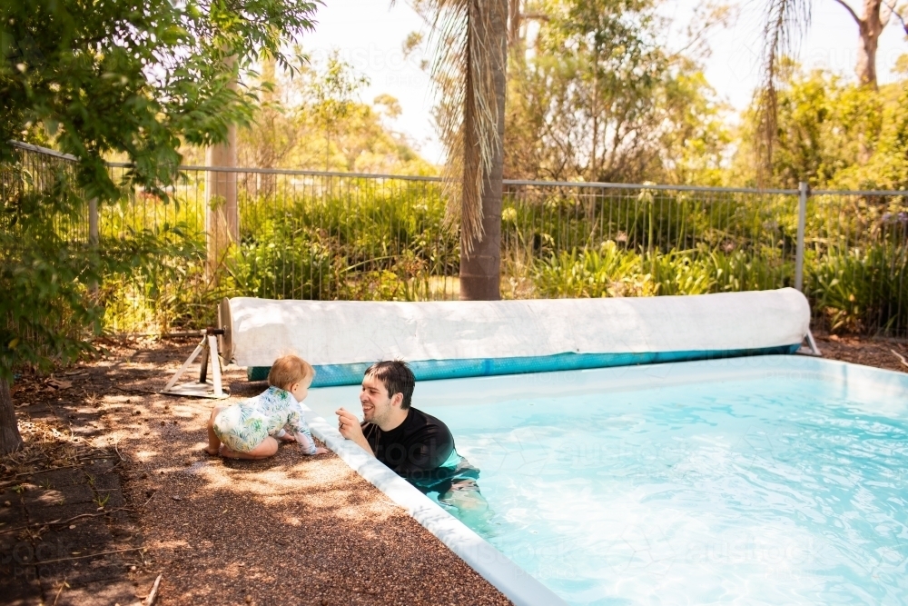 Happy man with baby at the edge of an inground swimming pool in backyard - Australian Stock Image