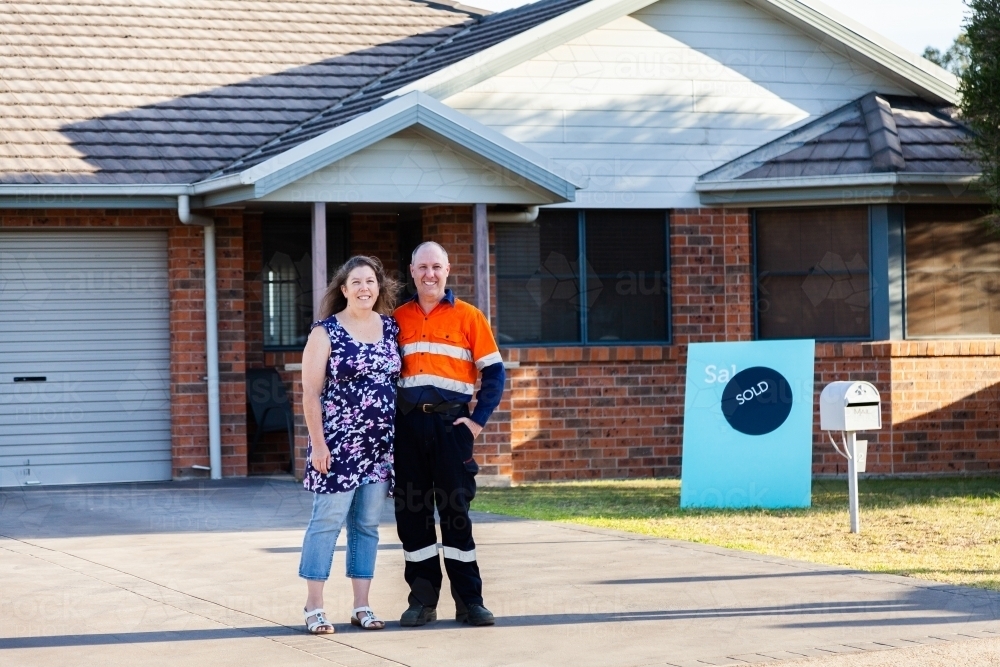 Happy middle aged couple smiling with newly purchased house sold sign - Australian Stock Image