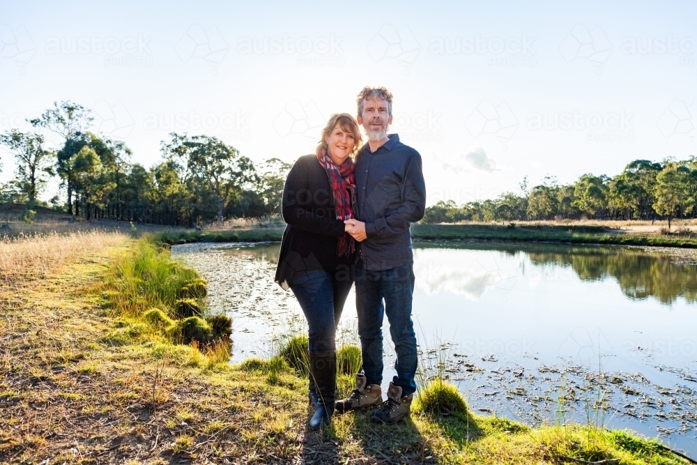 Happy middle aged couple together on farm beside dam - Australian Stock Image