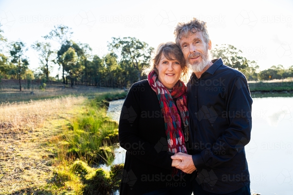 Happy middle aged couple together on farm beside dam - Australian Stock Image