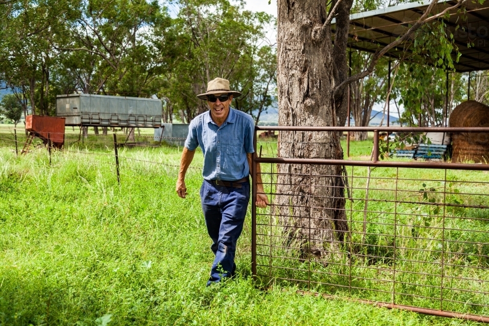 Happy middle aged farmer opening gate to paddock - Australian Stock Image