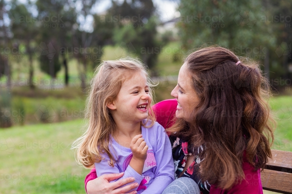 Happy mother and daughter laughing and giggling together outside at park - Australian Stock Image