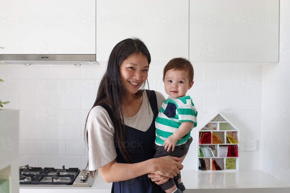 Happy mother holding baby boy in kitchen - Australian Stock Image
