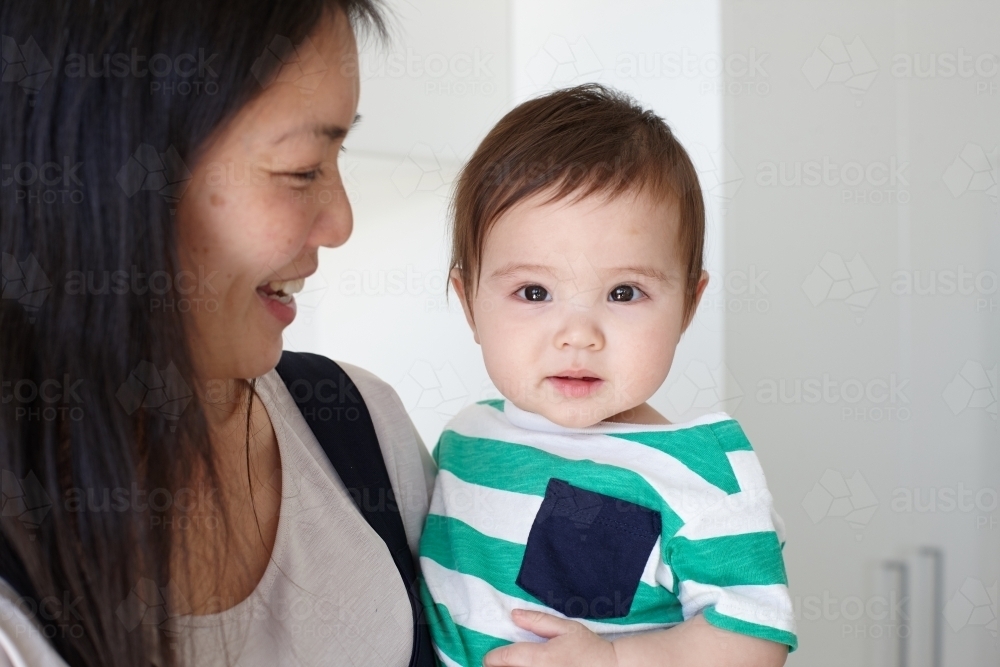 Happy mother holding baby boy in kitchen - Australian Stock Image