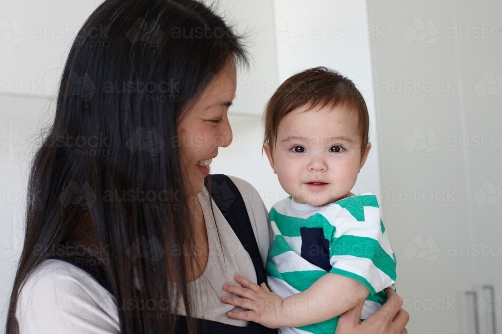 Happy mother holding baby boy in kitchen - Australian Stock Image