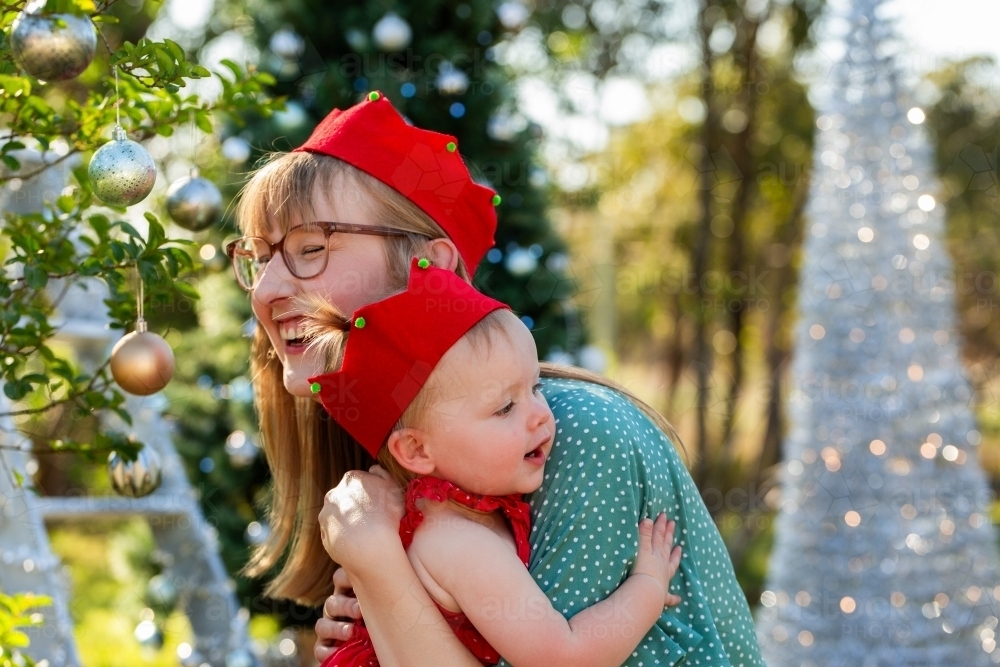 Happy mother with toddler daughter hug while wearing silly felt Christmas hats - Australian Stock Image