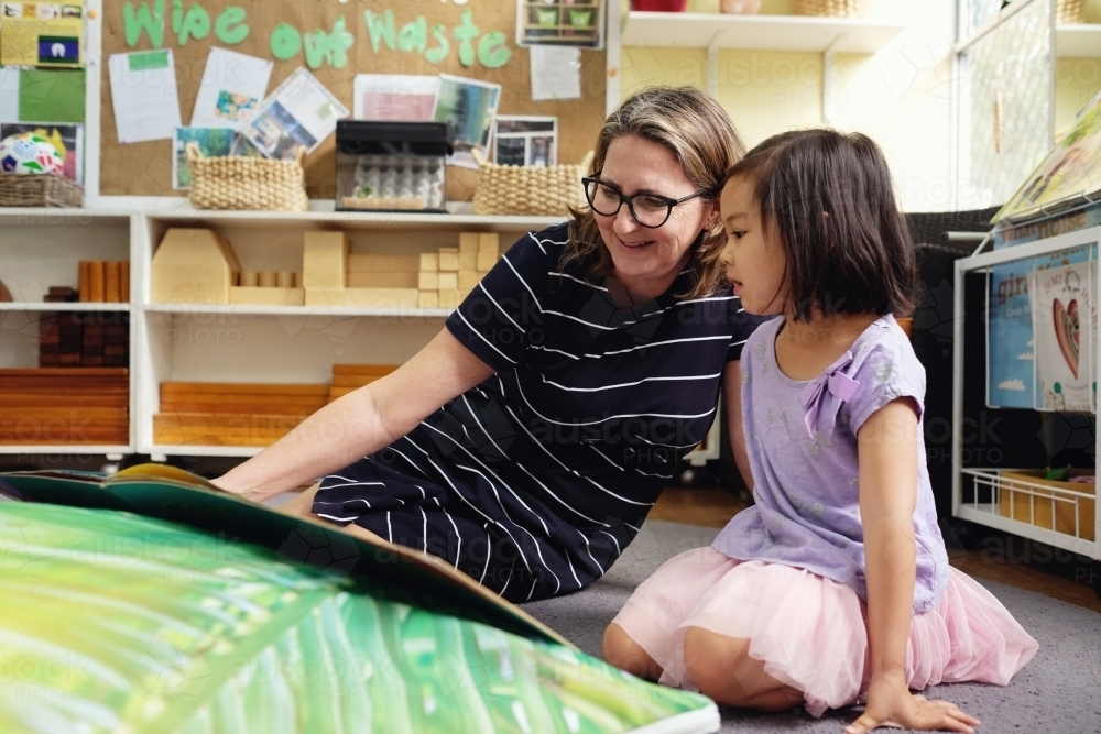 Happy multicultural teacher and child reading a book in kindergarten - Australian Stock Image